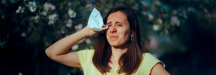 A woman squinting her eyes while holding a tissue.
