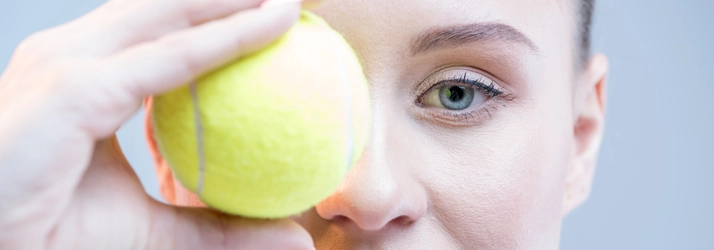 A woman holding a tennis ball over her eye.
