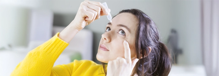 A woman putting eye drops in.